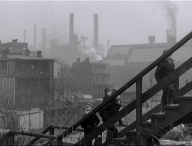 A still from Pittsburgh suggest the diversity of styles on display in the film. This one features an industrial backdrop and people ascending stairs.