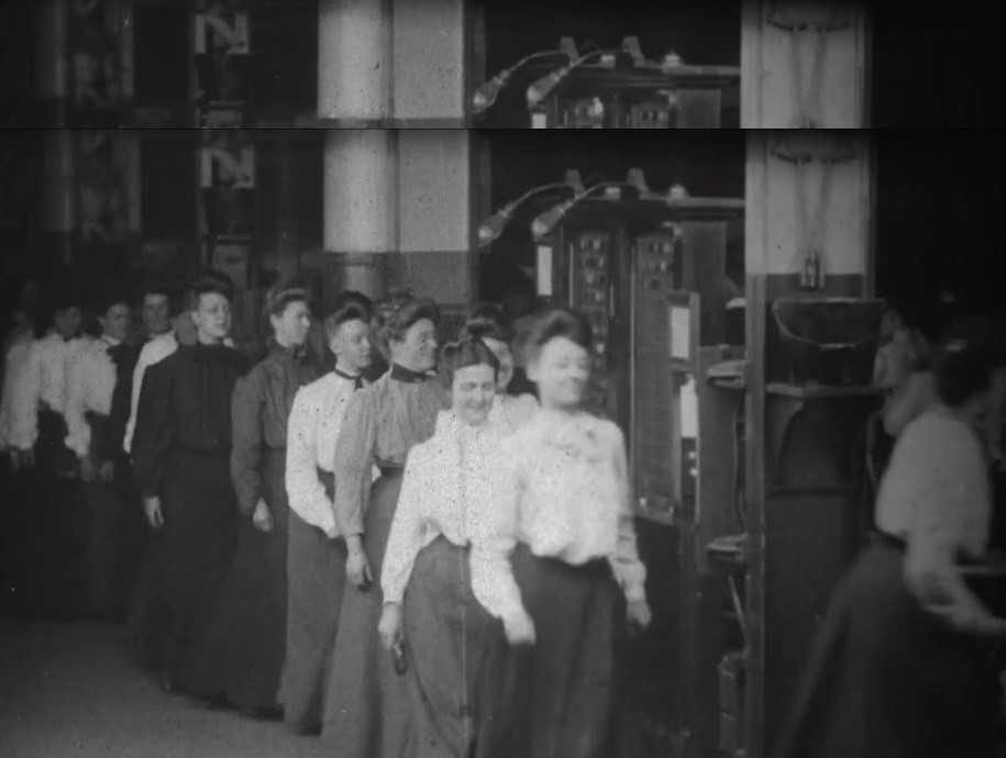 A still from Girls Taking Time Checks, part of the Westinghouse Works series. Women are lined up in an industrial setting.